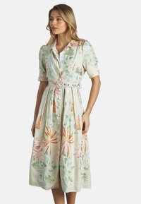 Vestito di colore chiaro, ricamato con fiori, con maniche corte, colletto e vita con cintura. Presenta bottoni lungo la parte anteriore e una gonna fino al ginocchio.