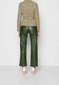 Veste en cuir beige avec taille ceinturée, associée à un pantalon large en simili cuir vert taille haute et des talons aiguilles blancs.