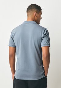 Šedé polo tričko s klasickým límcem a krátkými rukávy, s hladkou texturou a pohodlným střihem, zobrazené zezadu.