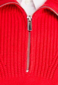 Maglione rosso a maglia con zip frontale in metallo, design a coste testurizzato e una camicia bianca sotto.