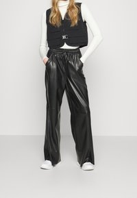 Czarne spodnie z szerokimi nogawkami z ekologicznej skóry, z elastycznym pasem i bocznymi kieszeniami, zestawione z dopasowanym białym prążkowanym topem i czarną krótką kamizelką.