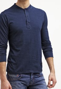 Námořnická dlouhá košile typu henley s kulatým límečkem, pěti knoflíky u krku a prošitým lemem. V kombinaci s modrými džínami.