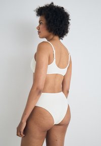 White bikini set with textured fabric. The top features adjustable straps and a simple back design, while the high-waisted bottom offers full coverage.