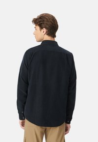 Camicia in corduroy blu navy con maniche lunghe, colletto button-down, orlo arrotondato e polsini. Presenta un tessuto testurizzato e una leggera lucentezza.