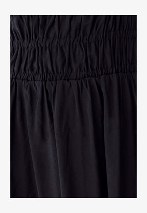 Mustast kangast, millel on elastne voltimine, mis loob kogutud, tekstuuriga horisontaalseid vöötmeid ja pehmet langevat kangast allpool.