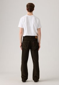Pantaloni din corduroy verde închis, cu un design drept, buzunare din spate parțial vizibile și o etichetă din piele maro pe talie.