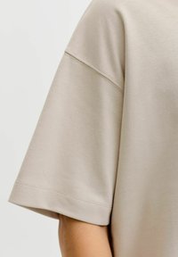 T-shirt en coton beige avec manches courtes, encolure ronde et détails de coutures discrètes sur l'ourlet et les coutures. Texture lisse.