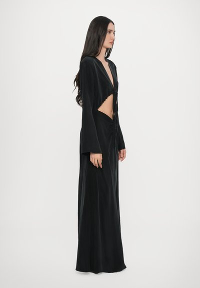 Robe en velours noir avec des manches longues, un décolleté en V profond et un détail découpé à la taille. Présente un lien à l'avant et une silhouette fluide.
