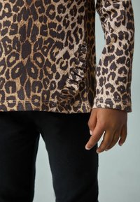 Langärmeliges Oberteil mit Leopardenmuster in gerippter Textur, mit ausgefranstem Saumdetail, kombiniert mit schwarzen Hosen.