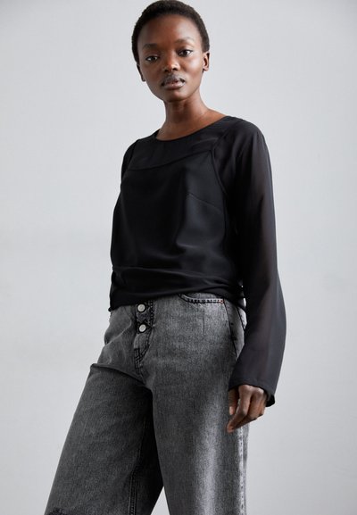 Blusa nera a maniche lunghe con texture liscia e scollo rotondo, abbinata a jeans in denim grigio a vita alta e dalla vestibilità ampia con chiusura a bottoni.