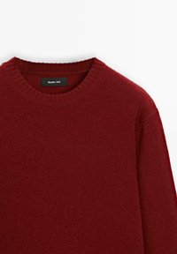 Červený pletený svetr s kulatým výstřihem, který má měkkou texturu a žebrovaný lem. Na štítku je napsáno "Massimo Dutti."