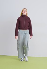 Bordo trumpas užtrauktukas džemperis su juodu logo, derinamas su šviesiai pilkų cargo kelnių, turinčių šonines kišenes ir elastingą juosmenį. Baltos sportbačiai.