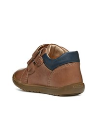 Scarpa in pelle marrone con un accento blu navy sul tallone, dotata di un cinturino in velcro e una suola in gomma testurizzata, progettata per il comfort.