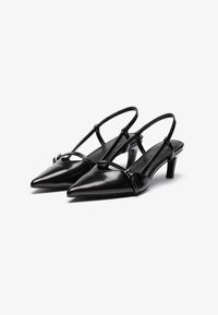 Svart lackläder slingback-skor med spetsiga tår, smala remmar och låg klack. Har metalliska detaljer på den främre remmen.