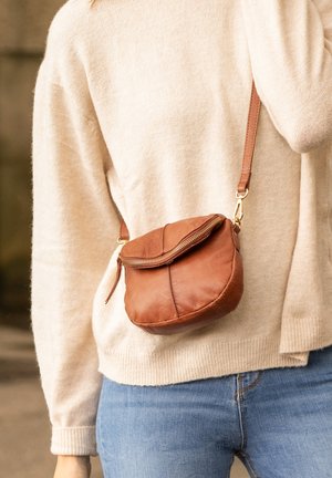 Brown leather crossbody bag with a rounded shape, top zipper closure, and adjustable strap. Soft texture with visible stitching details.