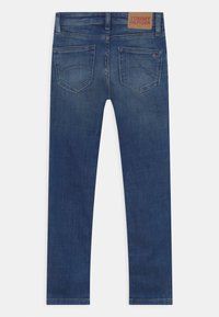 Jeans in denim con una tonalità blu scuro e una vestibilità slim. Presentano una patch in pelle marrone e due tasche posteriori con un design cucito.