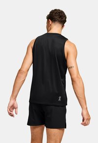 Top sportivo nero senza maniche con una texture liscia, con un logo sulla parte inferiore destra e una vestibilità comoda, abbinato a pantaloncini neri.