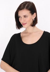 Top negru cu decolteu rotund, cu maneci scurte și largi, textura netedă și croiala lejeră, având un design simplu fără modele sau accente vizibile.