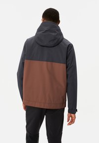 Giacca con cappuccio che presenta una parte superiore blu navy e una parte inferiore marrone, realizzata in un tessuto liscio e resistente all'acqua con polsini elasticizzati.