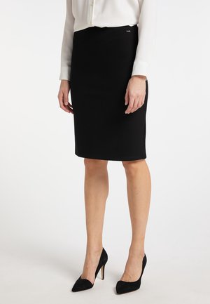 Woman wearing a black knee-length pencil skirt, white long-sleeve blouse, and black pointed high heels standing against a plain background.