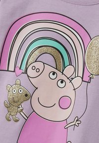 Lila shirt met een cartoon varkenskarakter in een roze jurk, die een gouden glinsterende ballon vasthoudt en een bruine karakter, met kleurrijke regenbogen.