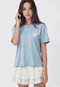 Světlomodr�é bavlněné tričko s krátkým rukávem, s malou bílou grafikou na hrudi. V kombinaci s bílou sukní s vrstvami a volány.