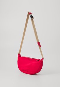 Borsa a tracolla in pelle fucsia con forma curva, dotata di chiusura con zip, tracolla beige e logo in rilievo sul frontale.