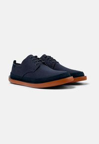 Navy canvas shoes with a smooth texture, rounded toe design, contrasting brown rubber sole, and six eyelet lace-up closure.