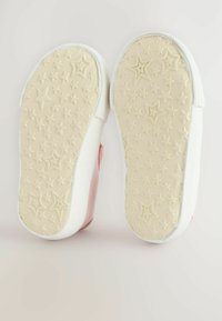 Semelle de sneaker rose avec des contours en caoutchouc blanc texturé. La semelle présente des motifs en forme d'étoile, offrant adhérence et traction.