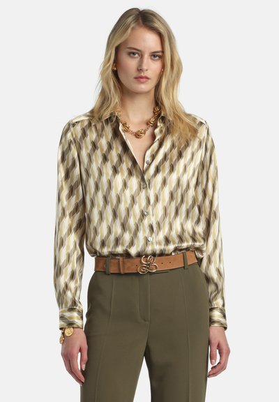Zijden blouse met een verlengd ruitpatroon in aardetinten, voorzien van een knoopsluiting aan de voorkant en lange mouwen. Gecombineerd met een bruine riem en groene broek.