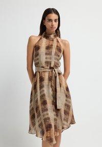 Halterneck jurk in een bruin en beige patroon, met een ceintuurlijn en een vloeiende zoom. Gemaakt van lichtgewicht stof, met een textuurdesign.