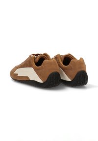 Zapatillas de ante marrón con un diseño de zigzag blanco en el lateral, suela de goma texturizada y punta redondeada. Talón reforzado y cordones suaves.