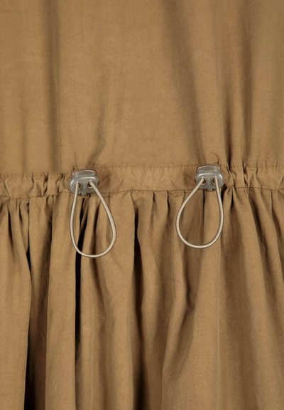 Tissu marron avec couture froncée et deux boucles en cordon élastique gris fixées près du centre sur un vêtement.