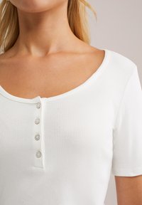 Weißes, geripptes Oberteil mit Rundhalsausschnitt, kurzen Ärmeln und vier Knöpfen entlang der Vorderseite. Glatte Stoffstruktur, figurbetontes Design.