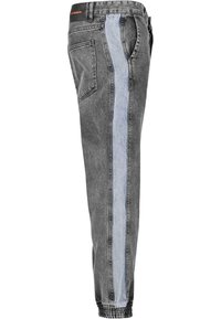 Pantalones de denim ajustados en negro con una raya vertical azul claro en el lateral y puños elásticos en los tobillos.