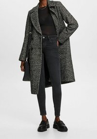 Mustakurkkuinen houndstooth-takki, jossa on yksirivinen malli, yhdistettynä mustiin slim-fit-farkkuihin ja mustiin loafer-kengiin. Tekstuuriset kangasvaikutteet näkyvät.