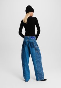 Denim wijde pijpen jeans, lichtblauw, met grote zakken en donkere patchaccents. Gecombineerd met een aansluitend zwart langemouwen shirt en een geribde beanie.