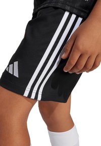 Pantalones cortos deportivos negros con tres rayas blancas a lo largo de los lados y un logo de Adidas, hechos de una tela suave y ligera.