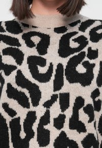 Pleteni pulover s bež pozadinom i velikim crnim uzorcima leoparda. Okrugli izrez i mekani materijal.