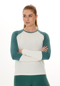 Langærmet atletisk top med en hvid krop og teal raglan ærmer. Fremstillet af et glat, letvægtsstof med en rund halsudskæring.