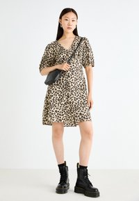 Φόρεμα με λεοπάρ σχέδιο, κοντά φουσκωτά μανίκια και κουμπιά, συνδυασμένο με μαύρες χιαστί μπότες και μια μικρή μαύρη τσάντα.