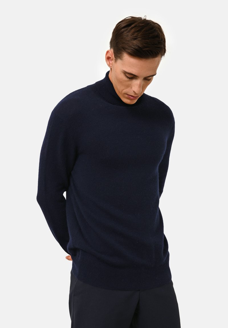 Navy high-neck sweater in soft fabric, featuring long sleeves and a relaxed fit, with ribbed cuff and hem details. Smooth texture.