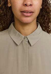 Khaki knap-op skjorte med klassisk krave, glat tekstur og en enkelt knap ved halsen. Har et minimalistisk design og let syning.