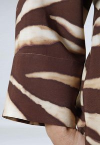 Brown and cream striped fabric showcasing a smooth texture; a folded sleeve with a clean hem and subtle stitching detail.