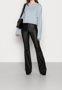 Pull court bleu clair à larges manches associé à un pantalon en cuir noir évasé taille haute, complété par un sac à bandoulière noir.