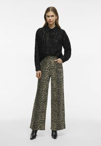 Melnas teksturētas džemperis ar apkakli, saskaņots ar plašām bēšām biksēm ar melnu leopardu rakstu. Melna, norādīta purngala potīšu zābaki.