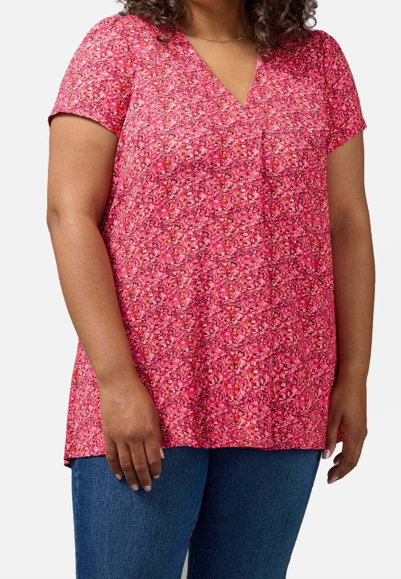 Floral v-neck top in pink with short sleeves, featuring small multi-colored flower patterns. Made of lightweight fabric with a relaxed fit.