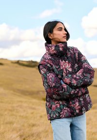 Gepolsterte Jacke mit dunklem Blumenmuster und hohem Kragen. Farbpalette umfasst Lila, Grün und Pink. Weiche, gesteppte Textur.