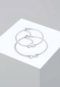Pulseras de cadena en tono plateado que presentan un símbolo de infinito, con eslabones delicados y un diseño minimalista. Un cierre ajustable en una de las pulseras.