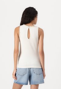 Top de tirantes blanco acanalado con espalda de ojete y adornos decorativos en los hombros. Combinado con pantalones cortos de mezclilla azul claros.